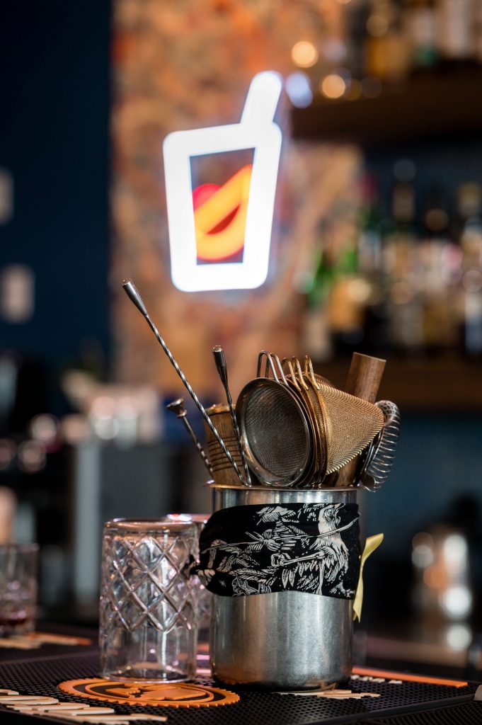 Bar tools in a tin beside the neon cocktail sign at the Gather bar