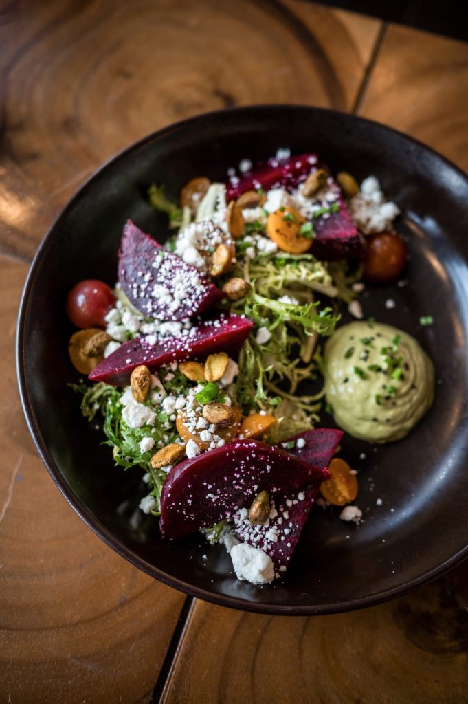 Roasted beet salad with greens, tomatoes and crumbled cheese in a black bowl