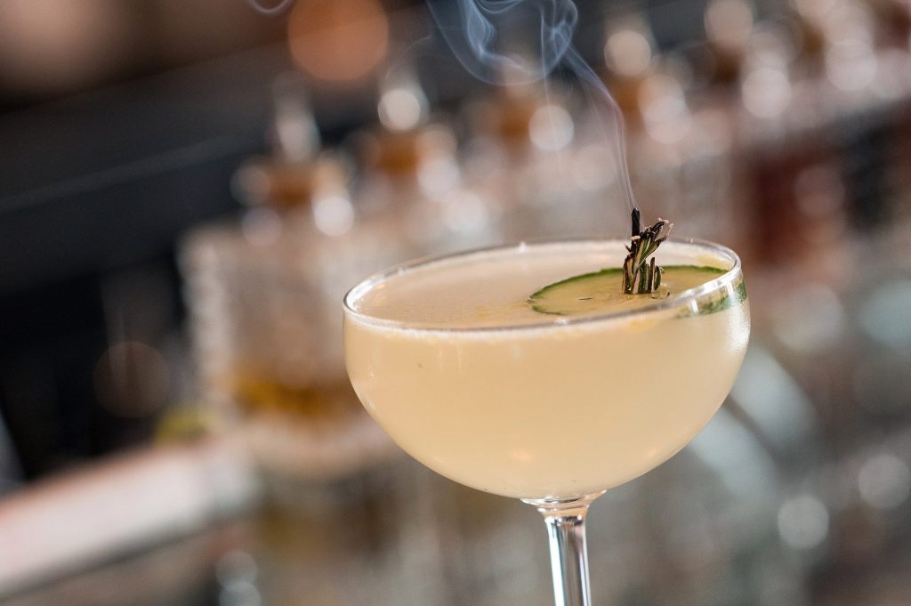 Coupe cocktail garnished with cucumber and a smoking herb sprig at the Gather bar