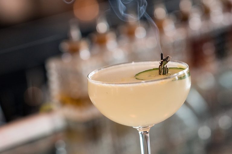 Coupe cocktail garnished with cucumber and a smoking herb sprig at the Gather bar