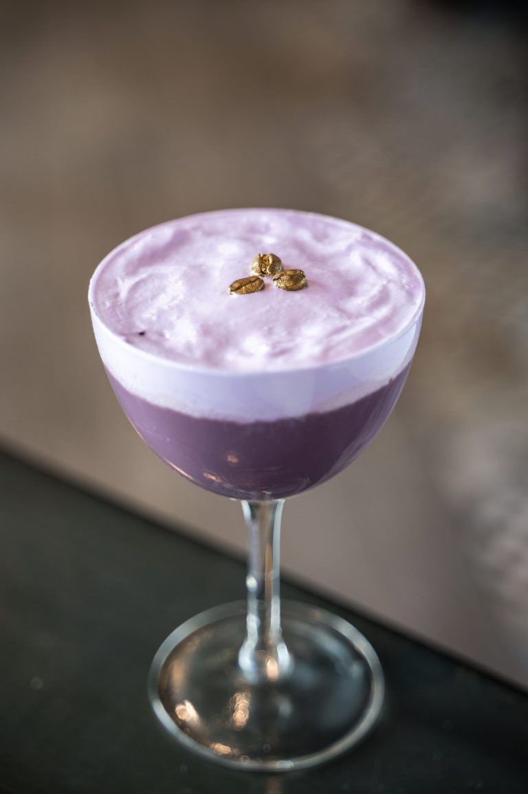 Purple coupe cocktail with a foamy top and gold coffee-bean garnish.