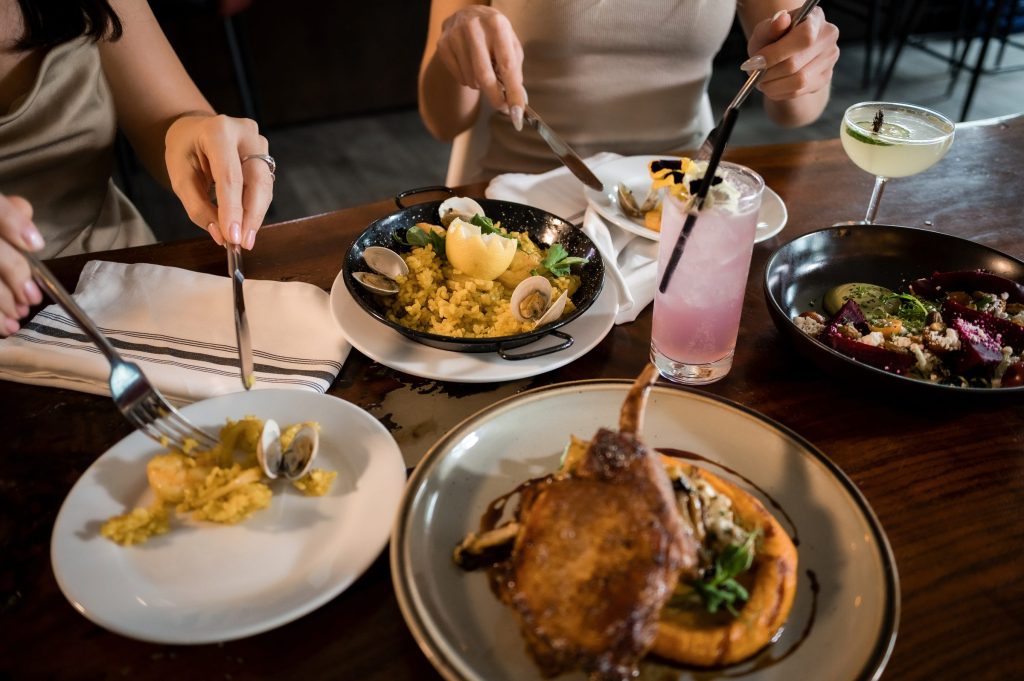 Guests sharing seafood paella, a chop and cocktails at a Gather table