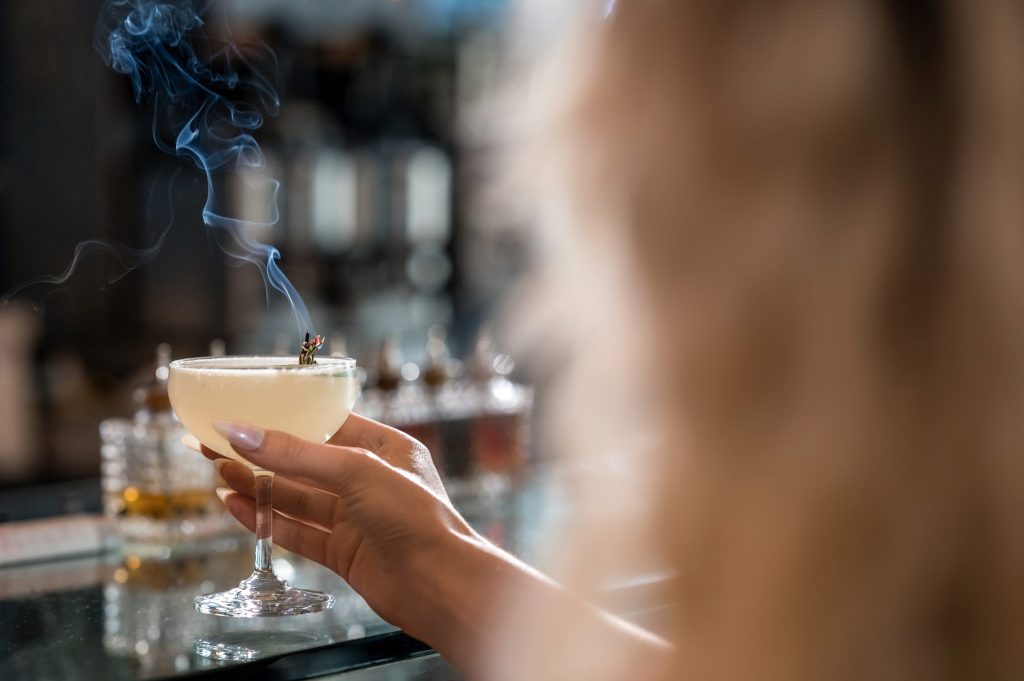 Guest holding a coupe cocktail with a smoking garnish at the Gather bar