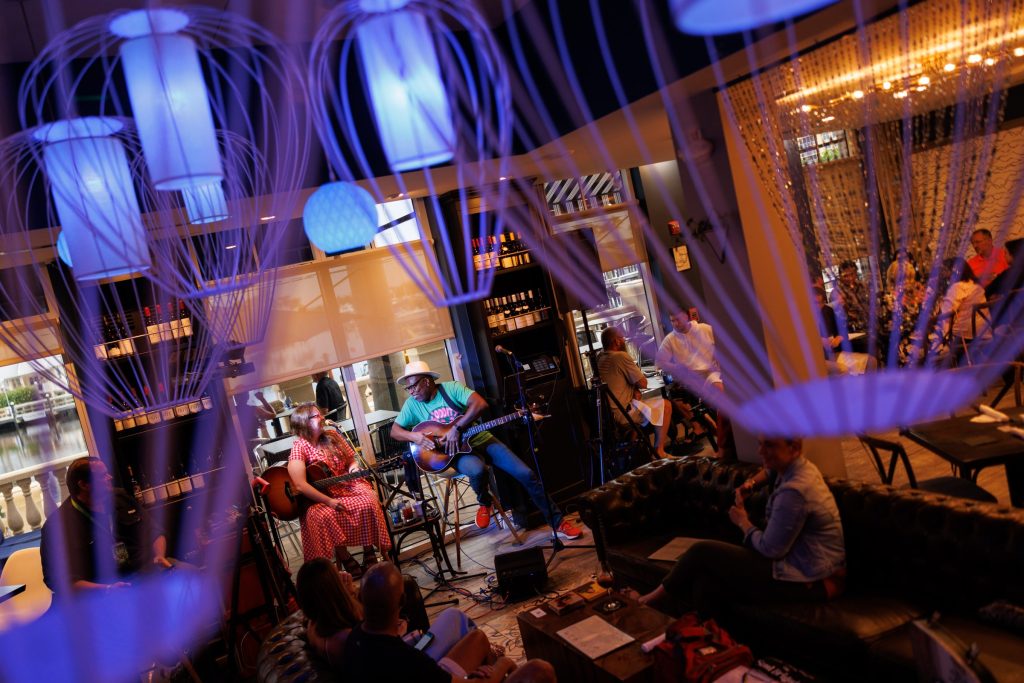 Two musicians performing live at Gather with guests seated around the stage.